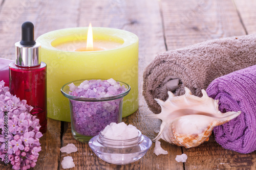Burning candle  bowls with sea salt  bottle with aromatic oil  lilac flowers and towels on wooden background.