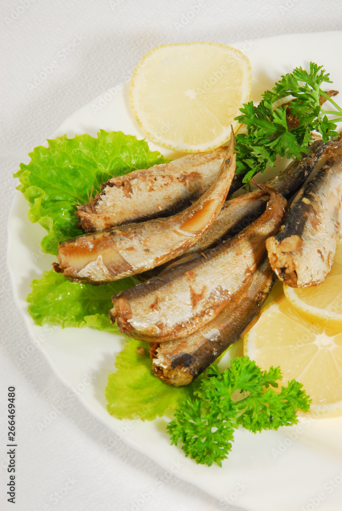 Pan-fried spiced sprats with lemon, salad on a plate Pan-fried spiced sprats with lemon, salad on a plate