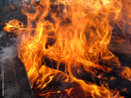 Firewood in flames, close-up. Yellow orange fire background, wooden boards are burning, with smoke
