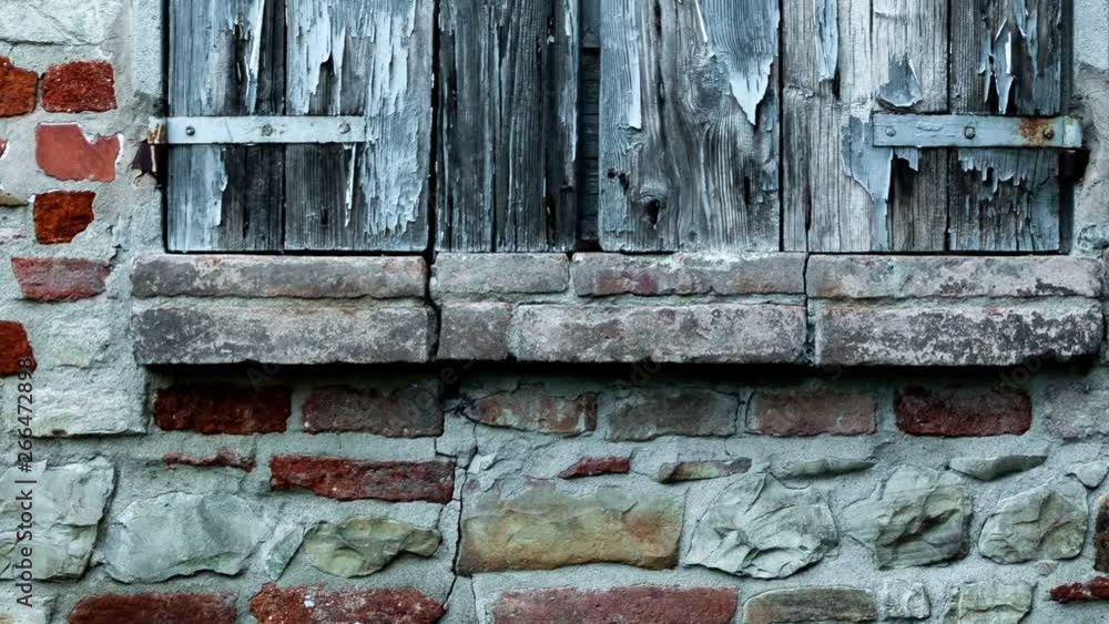 Window shutter of rural house, with brick wall and ancient stones. Damaged window with rusted iron hinges and cracked paint. Window shutter of rural house, with brick wall and ancient stones. Damaged window with rusted iron hinges and cracked paint.