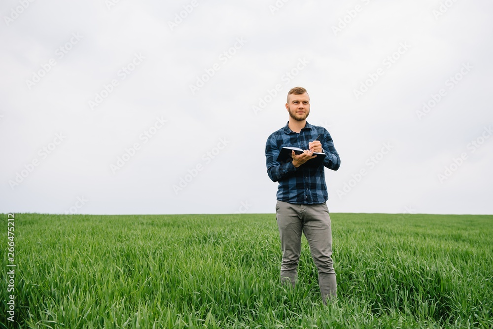 Young agronomist holds notebook in green wheat field. Agribusiness concept. agricultural engineer standing in a wheat field with a tablet in summer Young agronomist holds notebook in green wheat field. Agribusiness concept. agricultural engineer standing in a wheat field with a tablet in summer