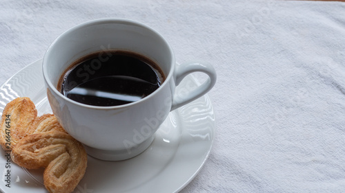 Cup of Greek or Turkish coffee  on small white saucer plate  with two cookie pastries  on white cloth surface