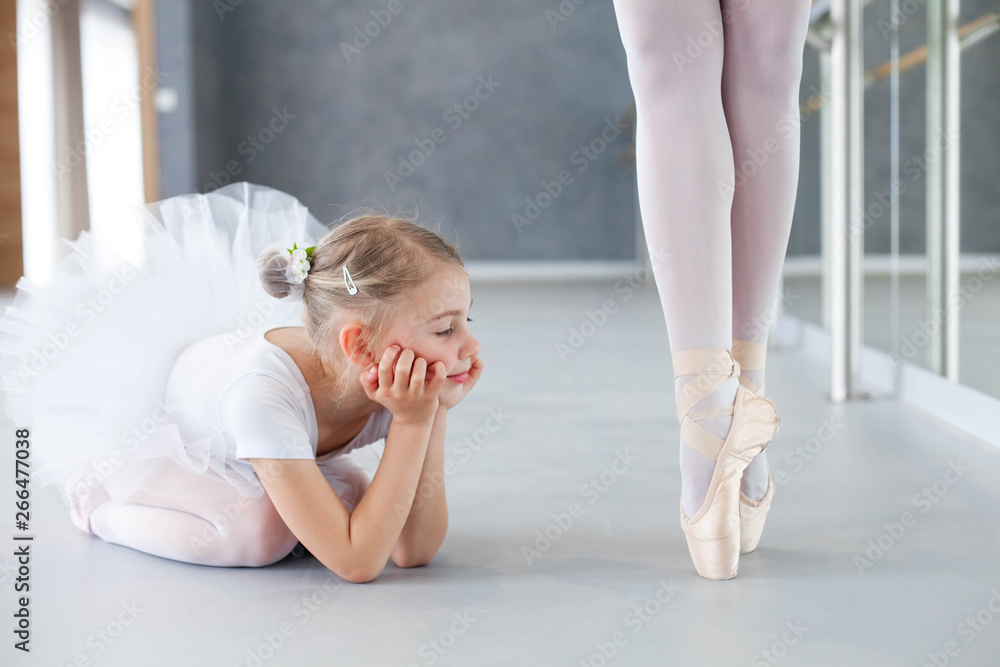 Little ballerina is looking at professional ballet dancer. Cute kid girl  dreaming of growing up. Adult dancing legs in ballet pointe shoes. Concept  of classical dance school, practicing for children. Stock Photo