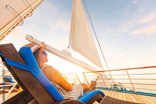 Luxury cruise vacation woman relaxing in lounger chair enjoying sunset on yacht deck with sail in wind sailing in getaway destination summer travel lifestyle. photo