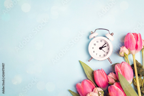 A bouquet of tulips and small roses with a white alarm clock on a blue background. Place for text.