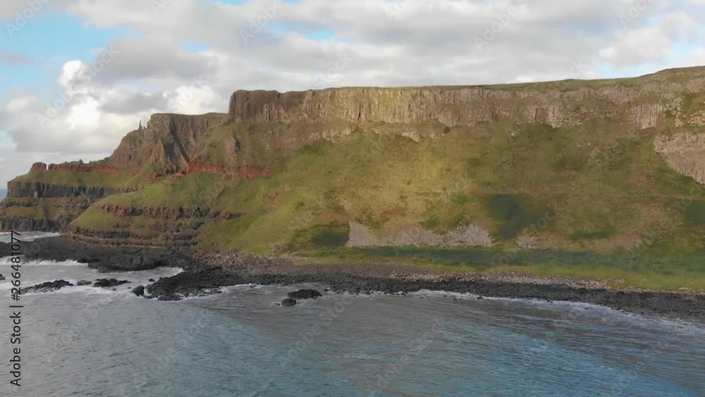 Low aerial shot of huge green cliffs and the rocky shore of Causeway Coast, Northern Ireland Low aerial shot of huge green cliffs and the rocky shore of Causeway Coast, Northern Ireland