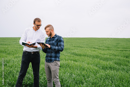Two farmer standing in a wheat field and looking at tablet  they are examining corp. Young handsome agronomist. Agribusiness concept. agricultural engineer standing in a wheat field