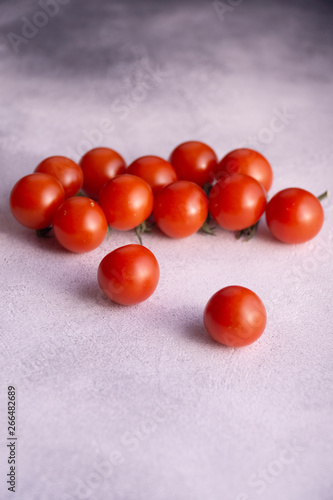 Bunch of cherry tomatoes on white stone concrete table, side view with copy space. Ingredients for cooking.
