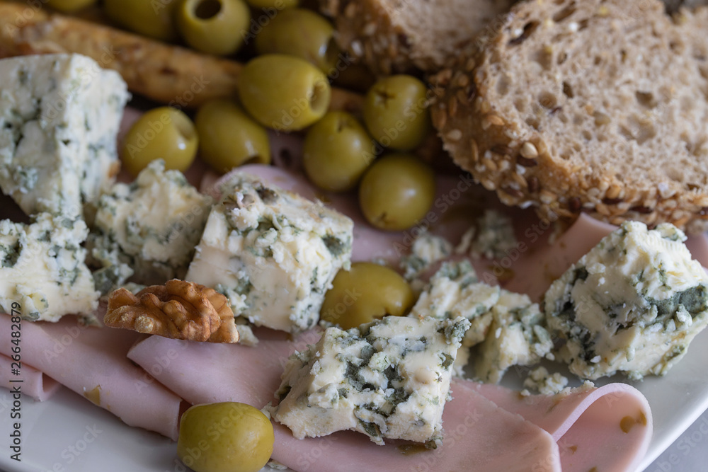 Wine snacks set. Blue cheese, Mediterranean olives, baguette slices, grissini, ham, grapes and different nuts on the plate. Tasty wine appetizer background. Close up