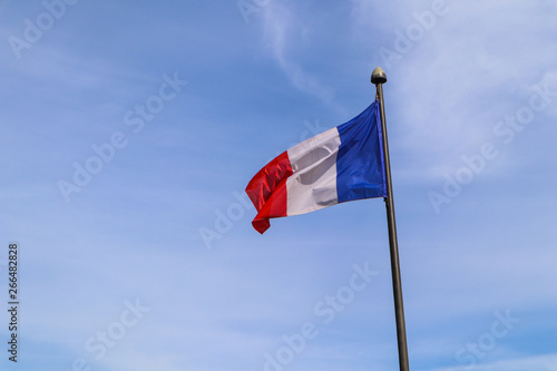 The national flag of France on the flagpole develops in the wind against the blue sky