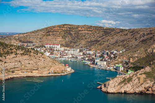 Aerial panoramic view of Balaklava bay in Crimea, mountain cliffs and sea with ships. Beautiful nature panorama landscape, town among hills and black sea coast from air