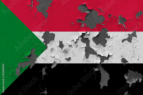 Close up grungy, damaged and weathered Sudan flag on wall peeling off paint to see inside surface.