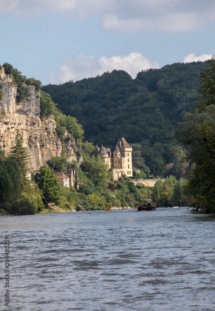  Canoeing and tourist boat, in French called gabare, on the river Dordogne at La Roque-Gageac and Chateau La Malartrie in the background. Aquitaine, France