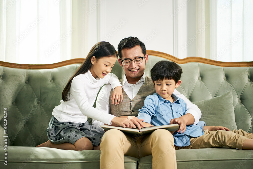 asian father and two children reading book together asian father and two children reading book together