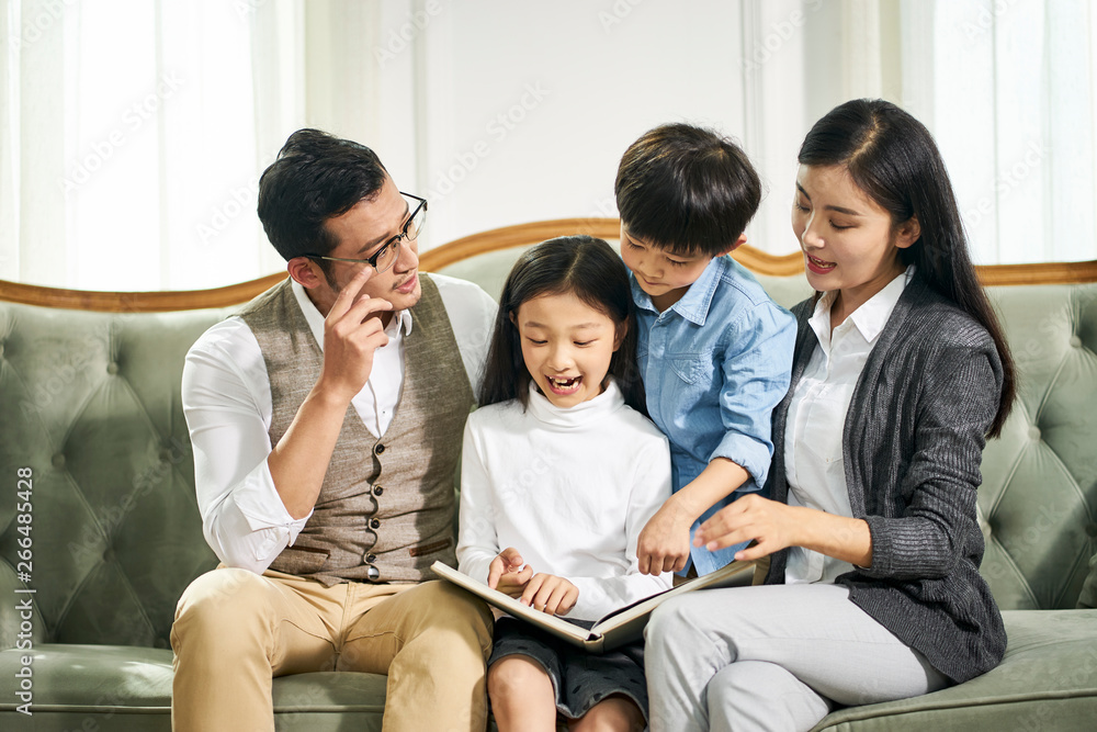 asian parents and two children reading book together asian parents and two children reading book together