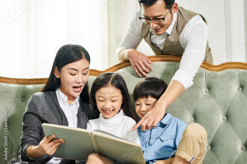 asian mother and father and two children reading book together
