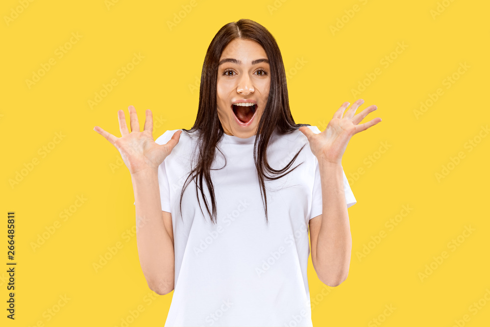 Happy smiling and surprised girl. Beautiful female half-length portrait isolated on yellow studio background. Young smiling woman. Negative space. Facial expression, human emotions concept. Happy smiling and surprised girl. Beautiful female half-length portrait isolated on yellow studio background. Young smiling woman. Negative space. Facial expression, human emotions concept.