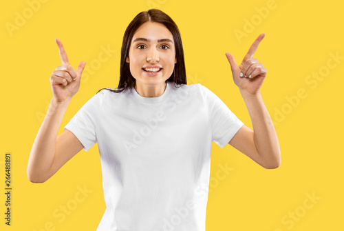 Happy smiling girl pointing up. Beautiful female half-length portrait isolated on yellow studio background. Young smiling woman. Negative space. Facial expression  human emotions concept.