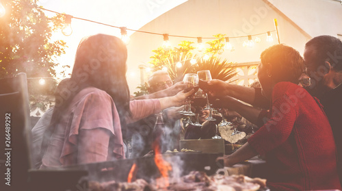Happy trendy family cheering with red wine at barbecue dinner outdoor - Different age of people having fun at sunday bbq meal - Food, taste and summer concept - Focus on people hands photo