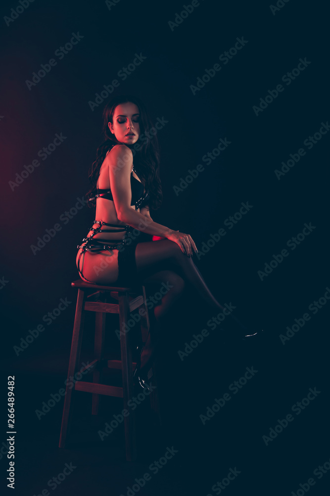 Vertical of nice lovely magnificent delicate attractive fit thin wavy-haired lady wearing swordbelt sitting on chair bar stool isolated over red light black background Vertical of nice lovely magnificent delicate attractive fit thin wavy-haired lady wearing swordbelt sitting on chair bar stool isolated over red light black background