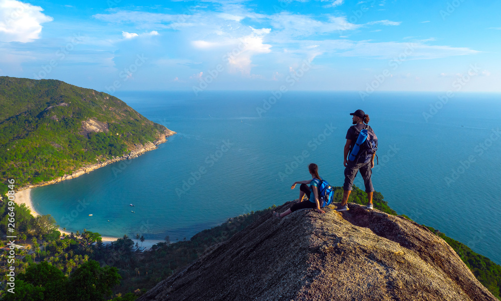 Man and woman stand on on top of cliff in summer mountains at morning time and enjoying view of nature