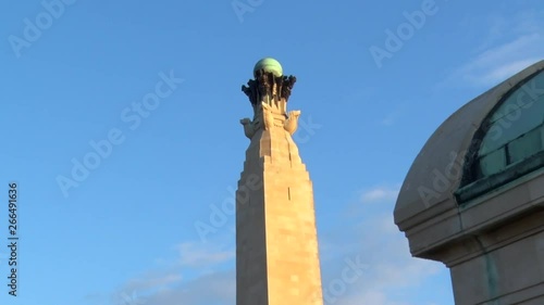 Zoom out reveal of the Portsmouth Naval War Memorial plinth with out building to the right from the North West side against a blue sky at sunset on a clear day.