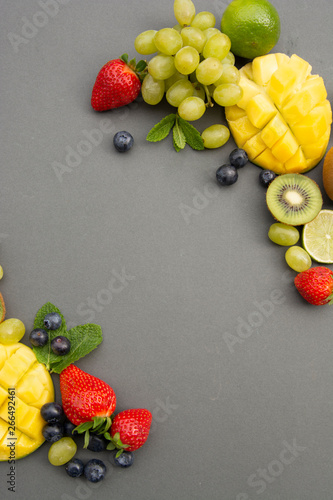 Fototapeta Naklejka Na Ścianę i Meble -  Creative layout made of summer fruits, frame. Tropical flat lay. Grapes, mango, strawberry, blueberry, kiwi, mint, lime, citrus fruits on blue background. Copy space.