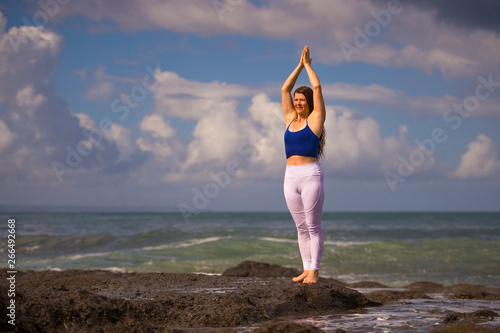 natural portrait of young beautiful and happy red hair woman practicing meditation and relaxation yoga lotus exercise standing at beach rock on the sea