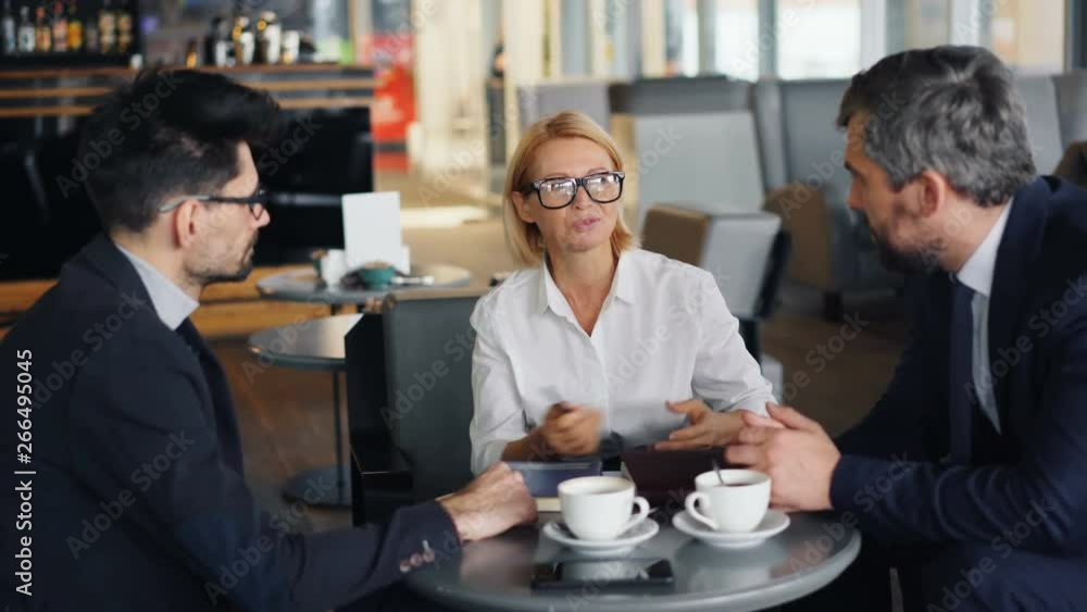 Smiling senior businesswoman is discussing work with male partners handsome men during informal meeting in cafe. Business, people and communication concept. Smiling senior businesswoman is discussing work with male partners handsome men during informal meeting in cafe. Business, people and communication concept.