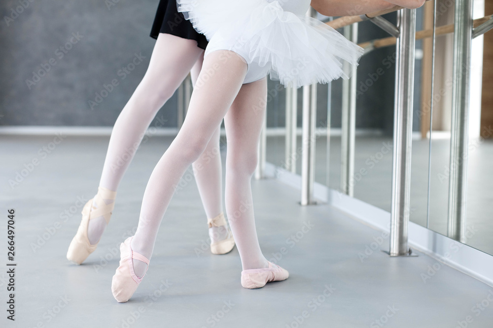 Two ballerinas child girl and woman in ballet pointe shoes. Little kid and  adult teacher are studying choreographic position for legs in front of  mirror in classical dance school. Close up. Stock