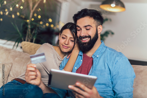 Smiling couple using digital tablet and credit card at home