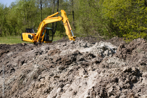 Big heap of soil with working excavator at the background at constructing new asphalt road at countryside near forest