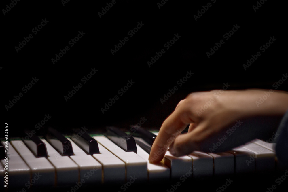 Fototapeta premium one male hand on the piano. The palm lies on the keys and plays the keyboard instrument in the music school. student learns to play. hands pianist. black dark background