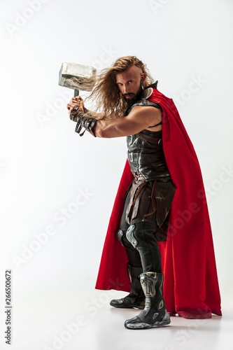 Fotografie Long hair and muscular male model in leather viking's costume with the big hammer cosplaying Thor isolated on white studio background