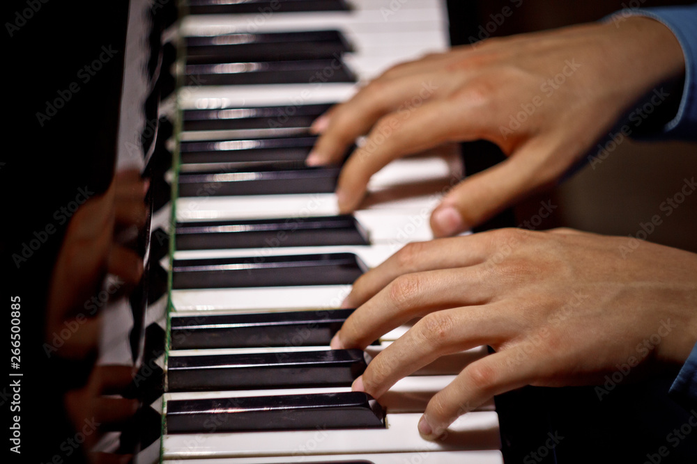 two male hands on the piano. palms lie on the keys and play the keyboard instrument in the music school. student learns to play. hands pianist. black dark background. top view