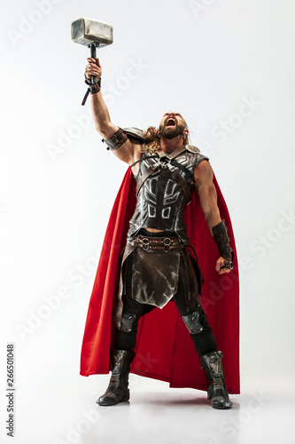 Long hair and muscular male model in leather viking's costume with the big hammer cosplaying Thor isolated on white studio background. Full-lenght portrait. Fantasy warrior, antique battle concept. photo