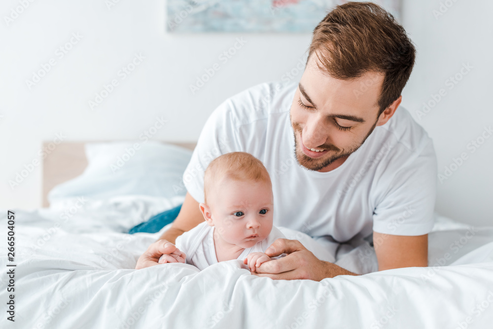 Smiling father lying on bed with baby in bedroom