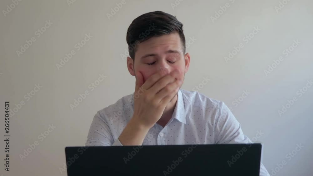 Young man sitting in front of computer tired and exhausted, yawning and rubbing face, medium still shot Young man sitting in front of computer tired and exhausted, yawning and rubbing face, medium still shot