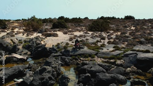 Drone panning shot of model sitting at an amazing paradise island beach Elafonissi, Crete photo