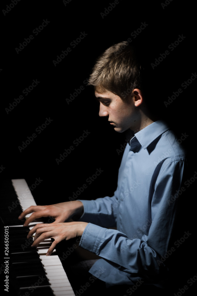 young man sitting at the piano. boy emotionally plays the keyboard instrument in the music school. student learns to play. hands pianist. black dark background. vertical young man sitting at the piano. boy emotionally plays the keyboard instrument in the music school. student learns to play. hands pianist. black dark background. vertical