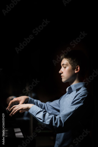 young man sitting at the piano. boy emotionally plays the keyboard instrument in the music school. student learns to play. hands pianist. black dark background. vertical