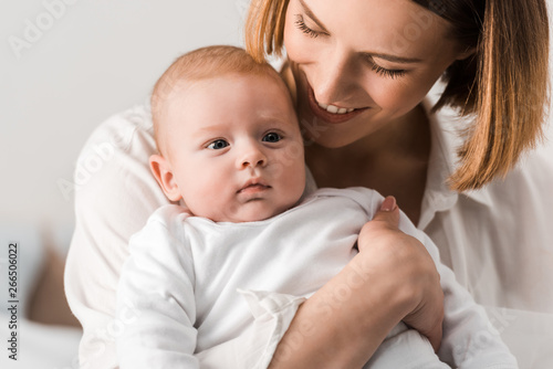 Smiling young mother in white shirt holding baby at home