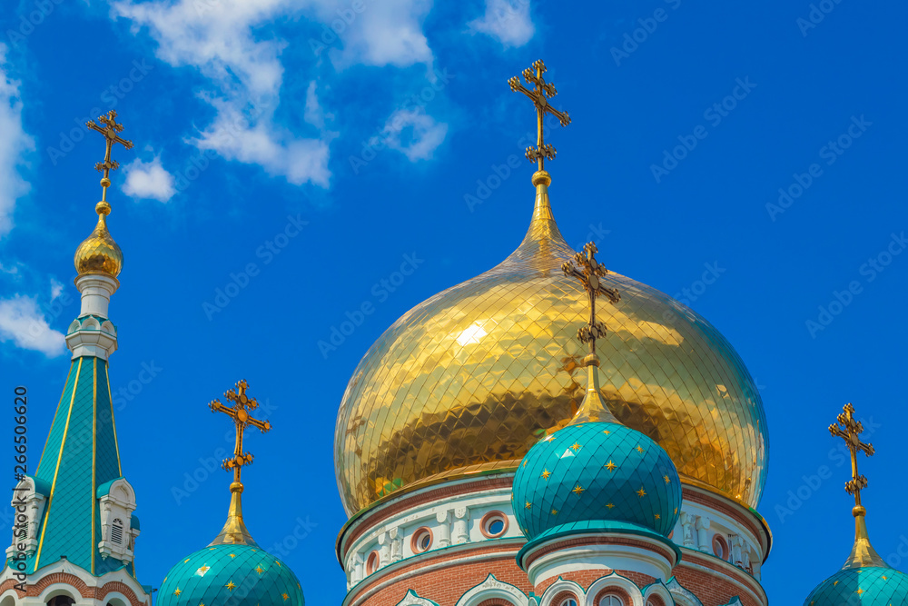 Domes of religious buildings. Crosses on the domes of the church. The cathedral with golden and green domes against the blue sky with clouds in the rays of the sun.