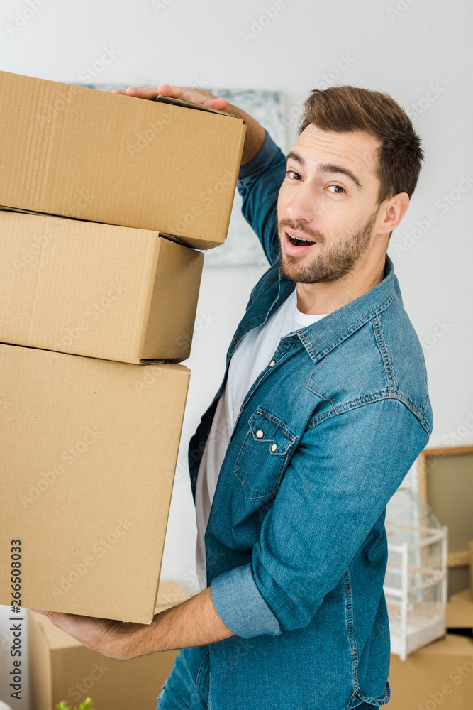 Joyful man in denim jacket holding cardboard boxes and looking at camera Joyful man in denim jacket holding cardboard boxes and looking at camera