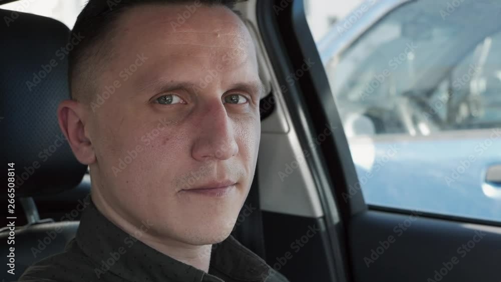 Portrait of a man sitting in a car. He looks at the camera.