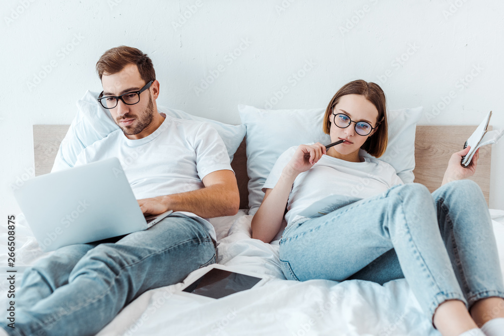 couple in glasses with laptop and notebook on bed couple in glasses with laptop and notebook on bed