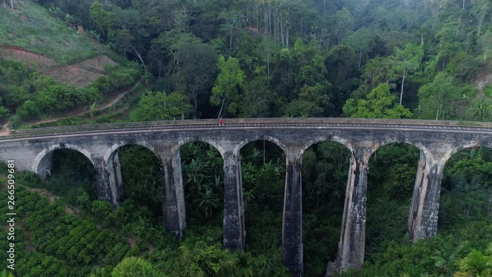 Woman in Red walks along tracks over arch stone bridge, Aerial 4k Woman in Red walks along tracks over arch stone bridge, Aerial 4k