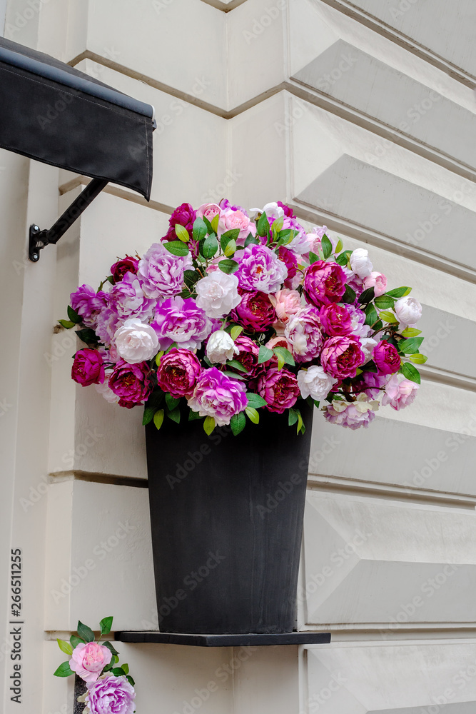 Artificial peony flowers in black vase on house facade
