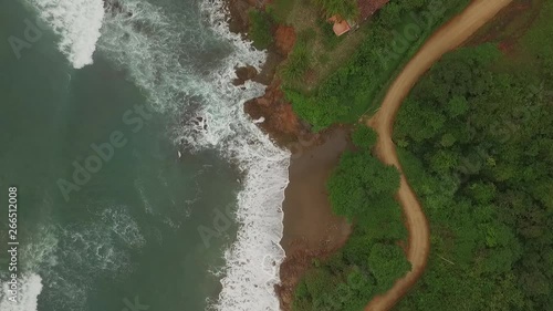 Aerial view of car driving on interesting dirt road between ocean waves and central american jungle. car drives top of scene to middle photo
