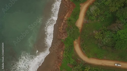 Aerial view of car driving on interesting dirt road between ocean waves and central american jungle. Car approaches scene from right. photo